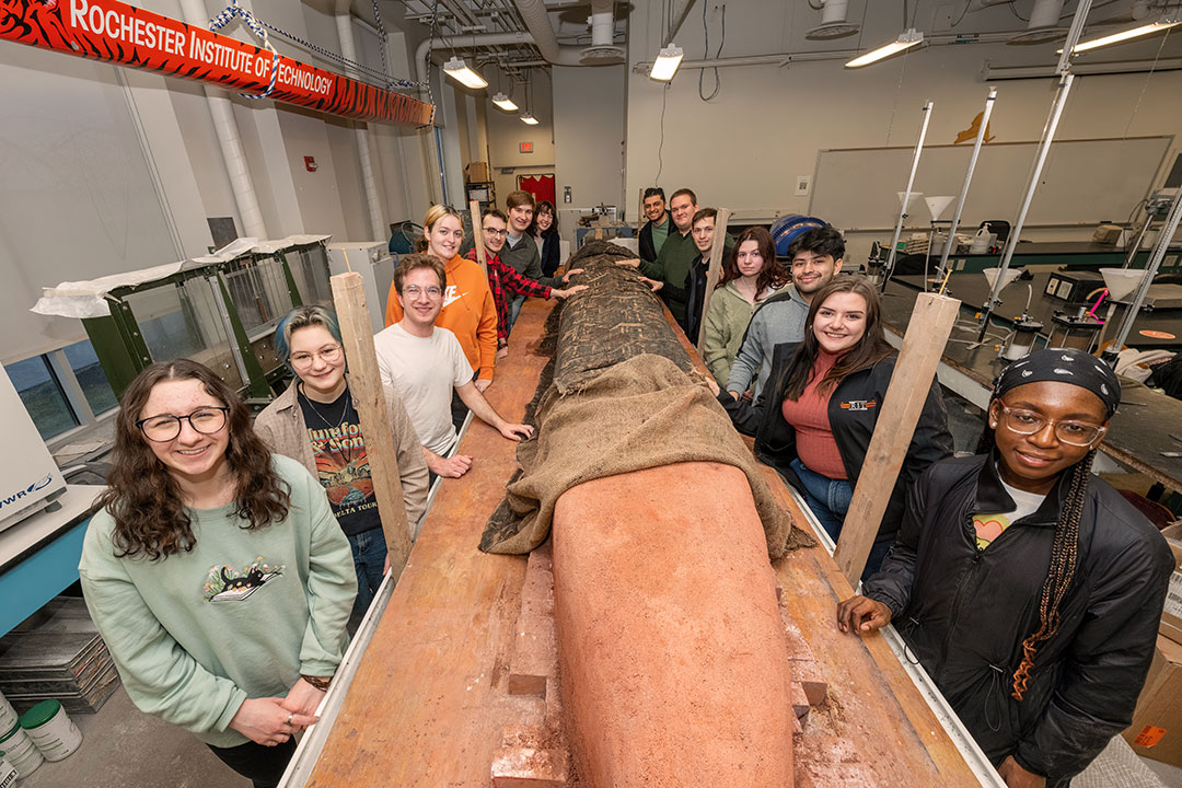 team of college students standing around a long concrete canoe.
