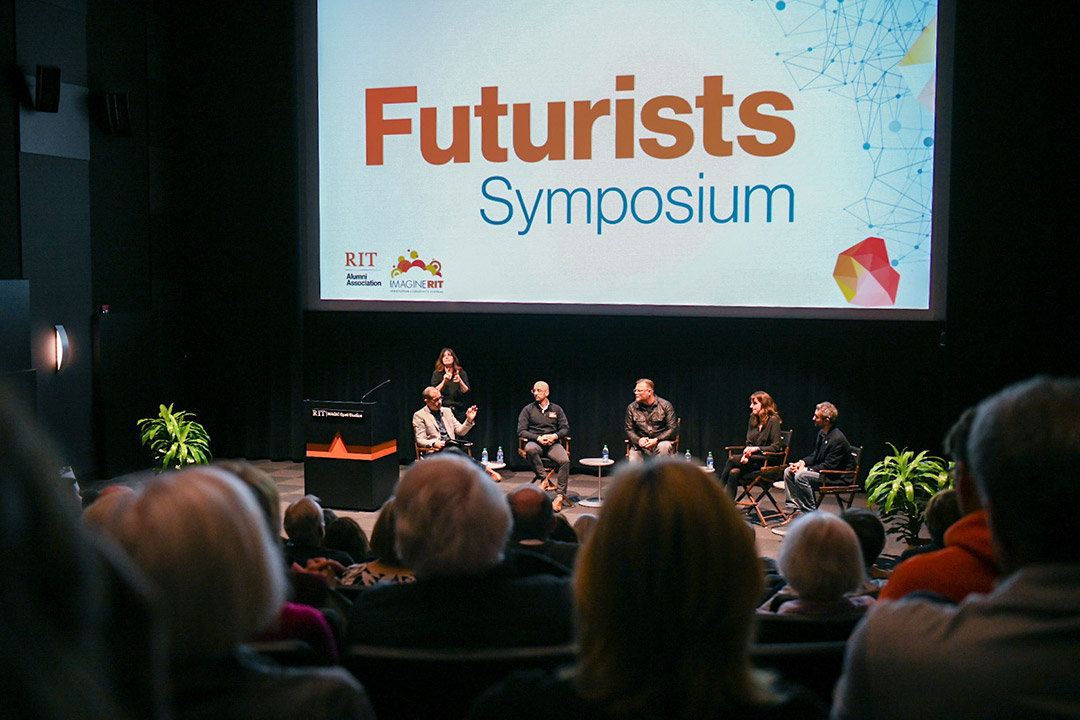 six people on a stage for a panel discussion with a projection above reading, Futurists Symposium.