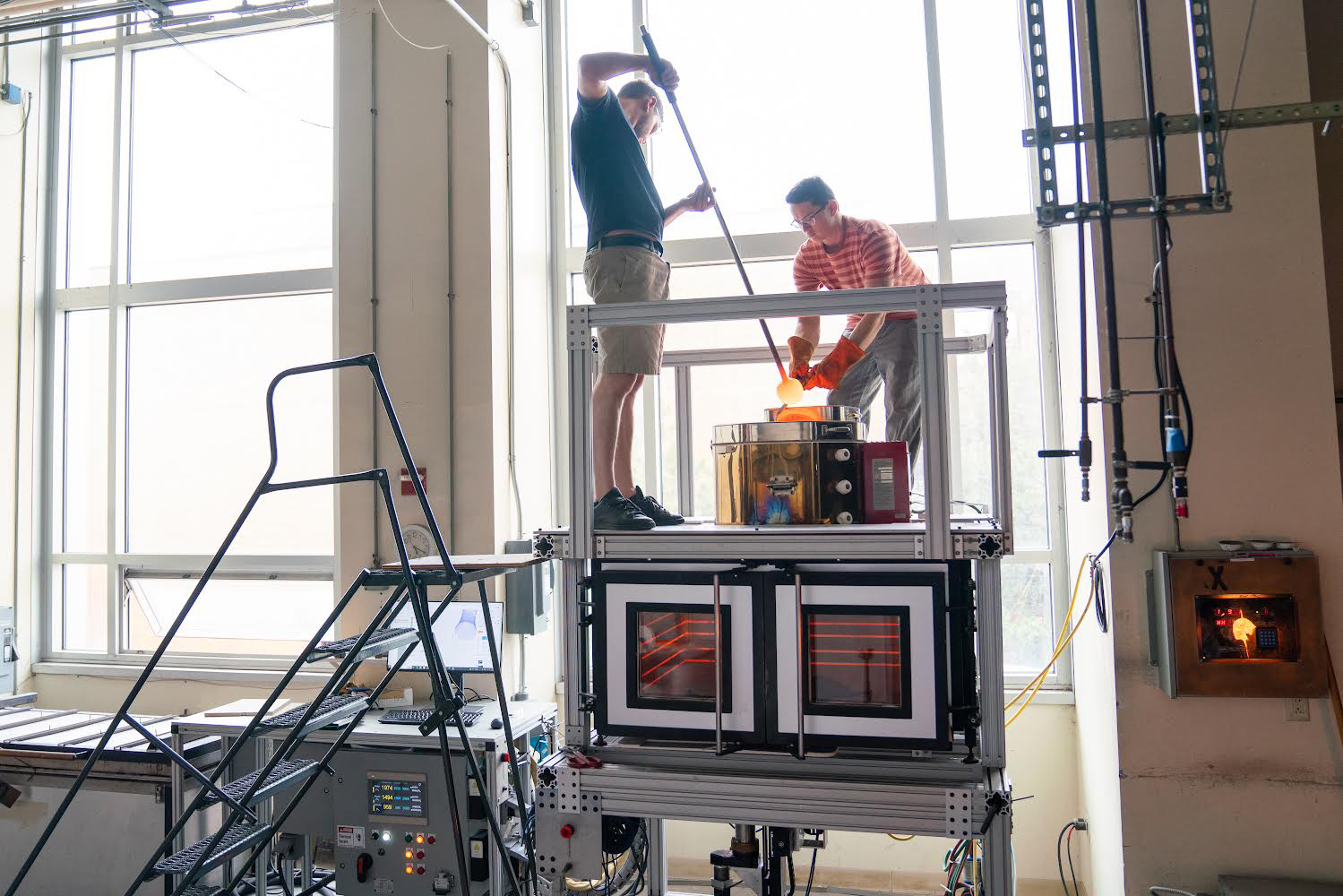 Michael Stern and Ethan Townsend load their molten glass 3D printer with hot glass to begin the printing process.