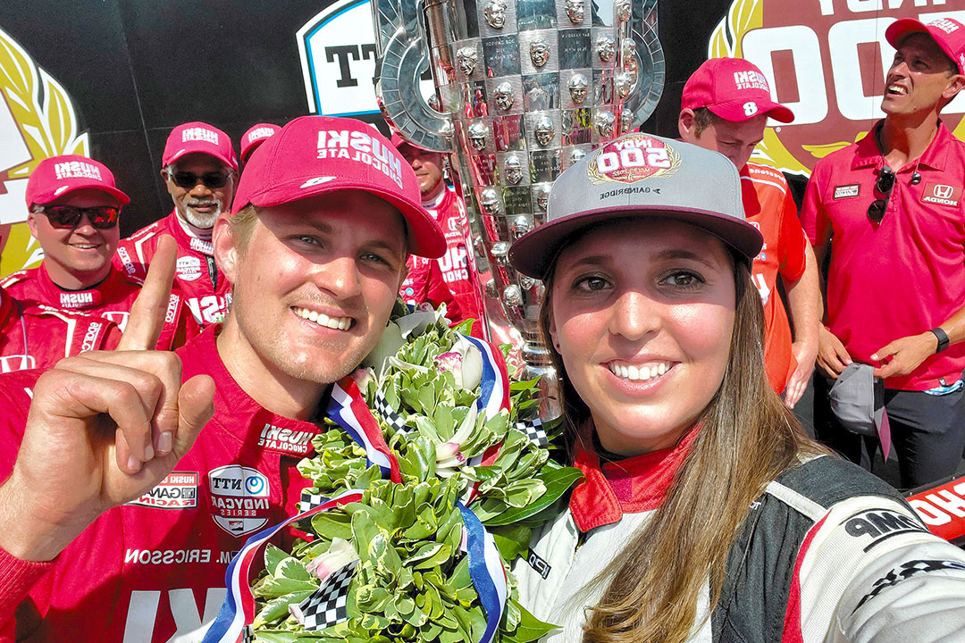 Two people wearing red pose with a trophy for a selfie.