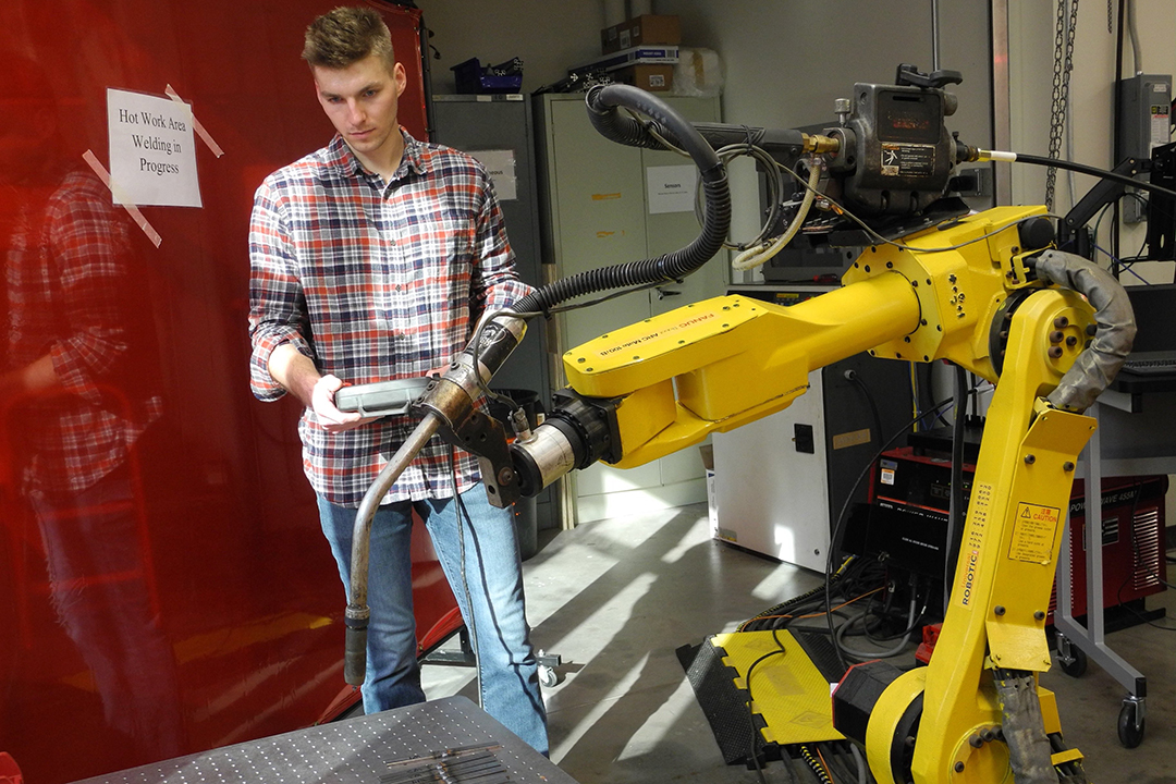 Pete Van Camp standing next to yellow robotics machine.