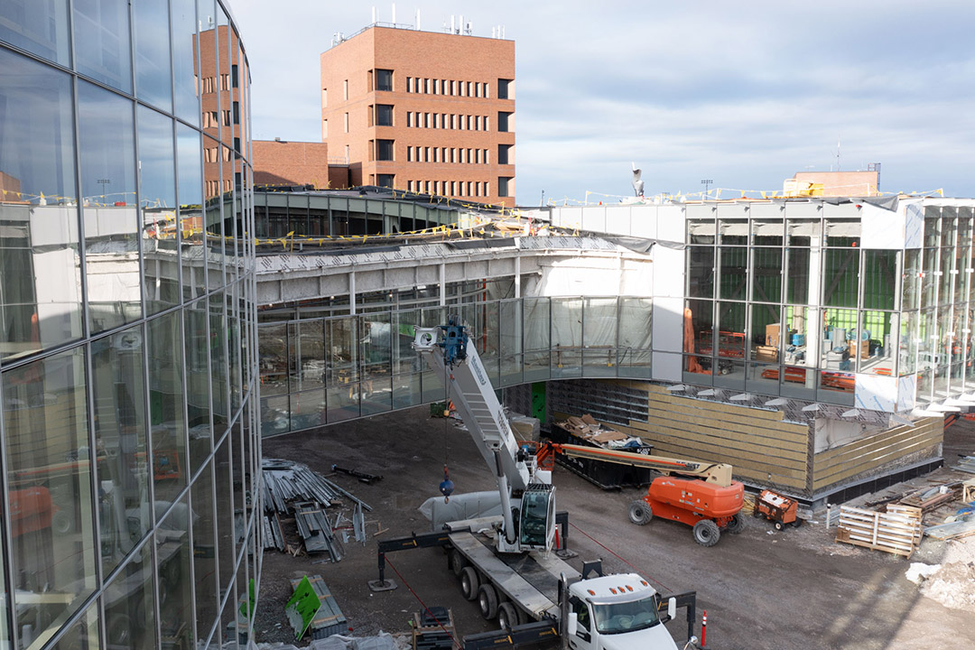 construction crews working on the exterior of a large glass building with a bridge over a walkway.
