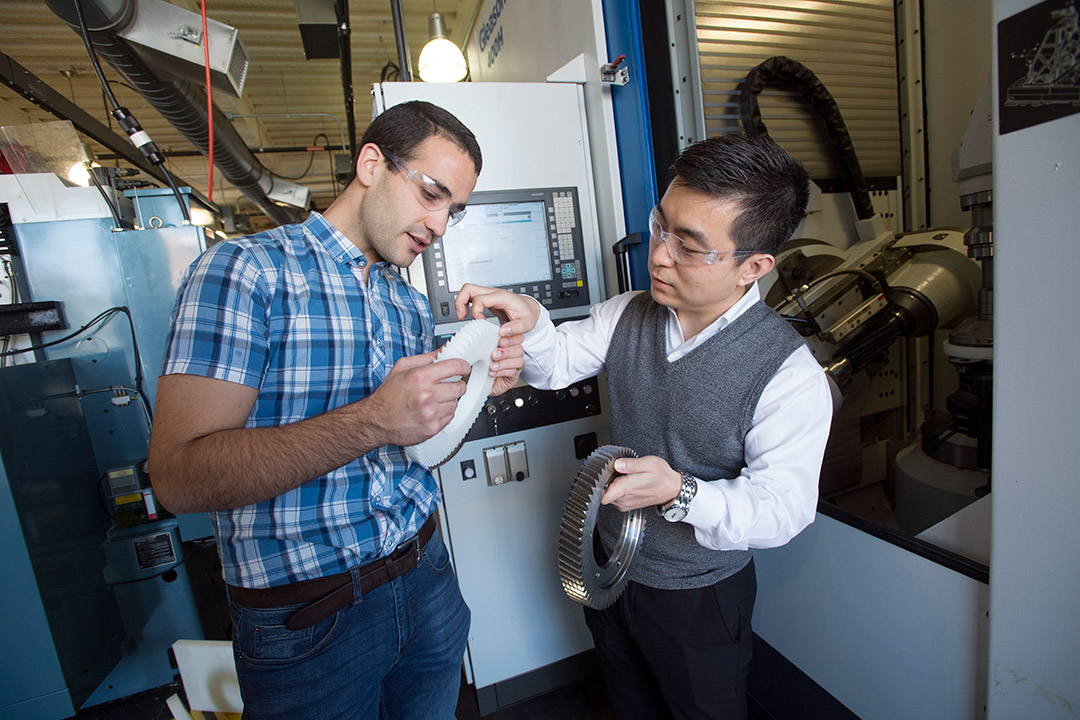 two researchers looking at a large, white gear.