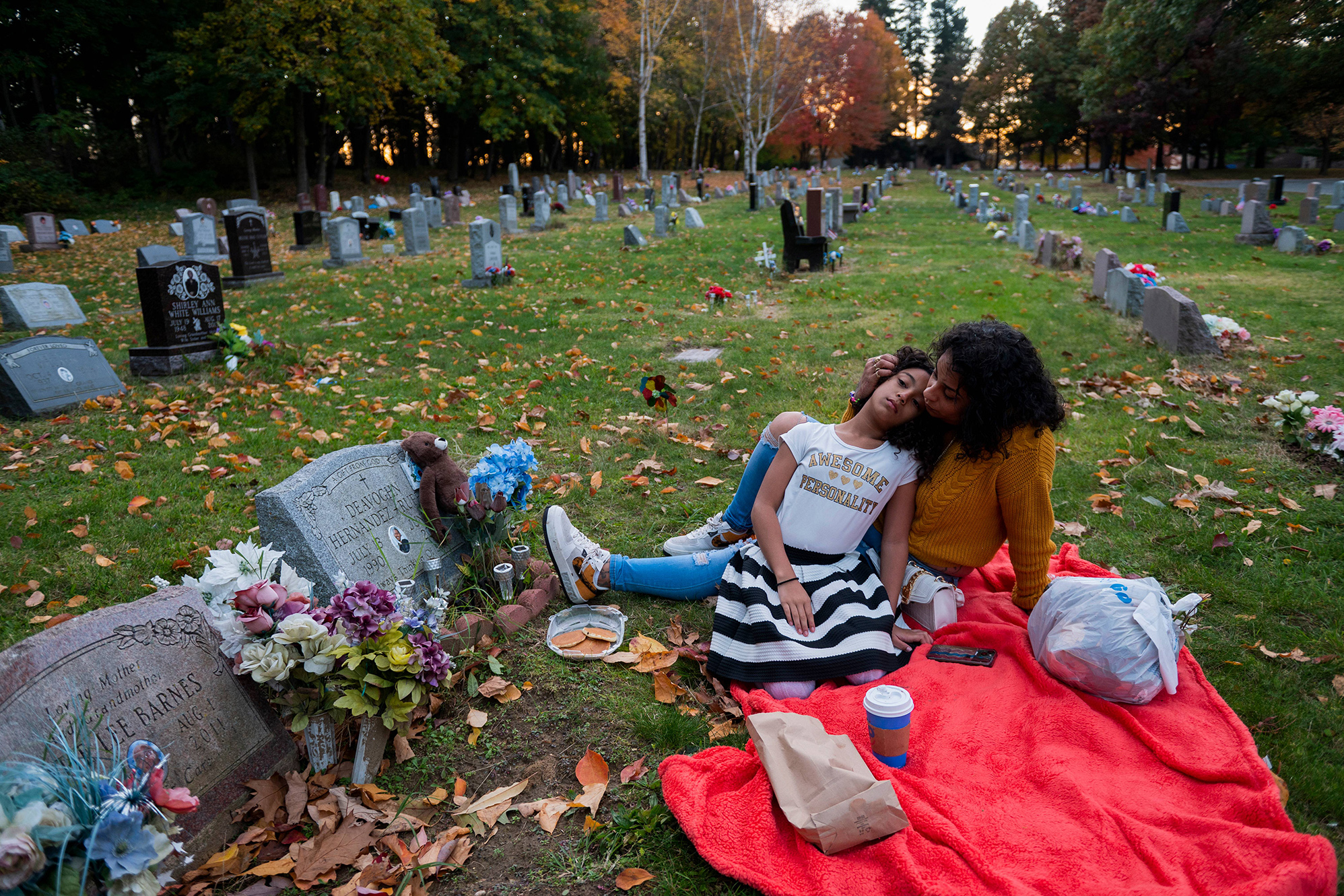 Two people embrace each other while laying on a blanket at a cemetery.