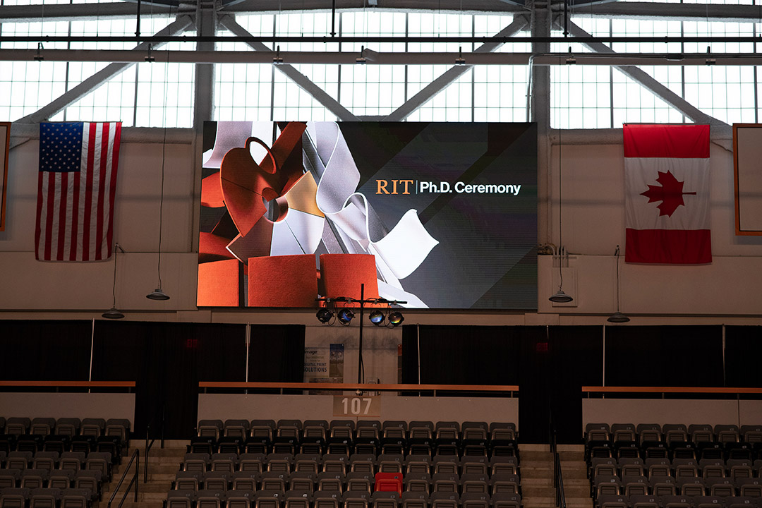 a sign between the American and Canadian flags that reads, R I T P H D ceremony.