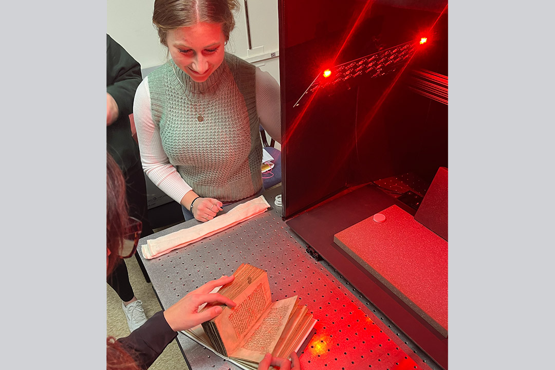 college student looking at an ancient book under special red lights.
