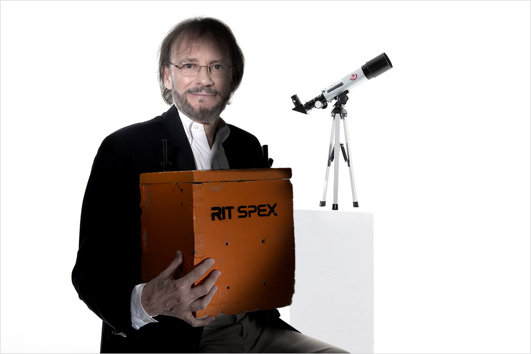 college professor holding an orange wooden box and has a telescope behind him.