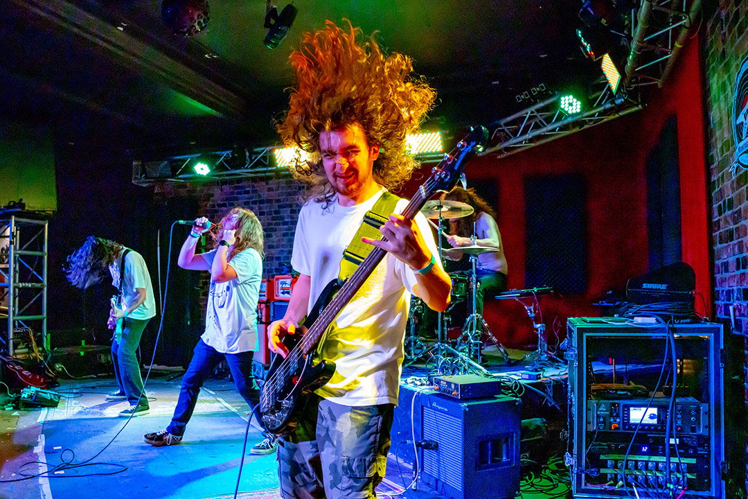 college student playing bass guitar on stage and flipping his hair up into the air.