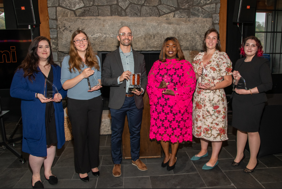 six people standing in front of a fireplace holding glass awards.