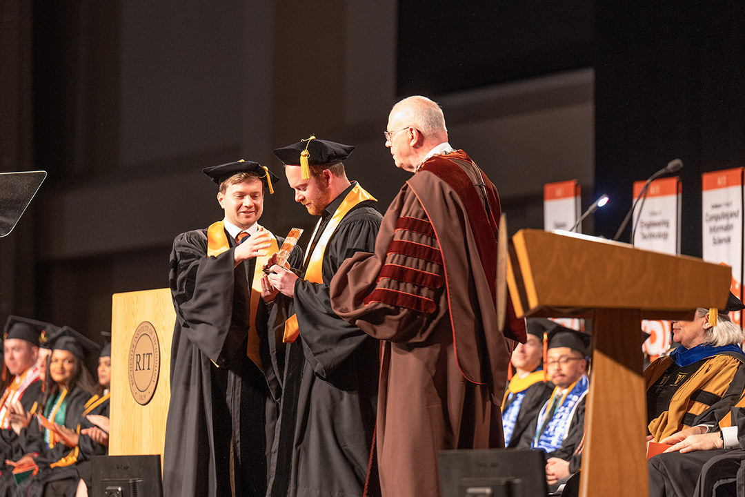 two people presenting a third with an award during a graduation ceremony.