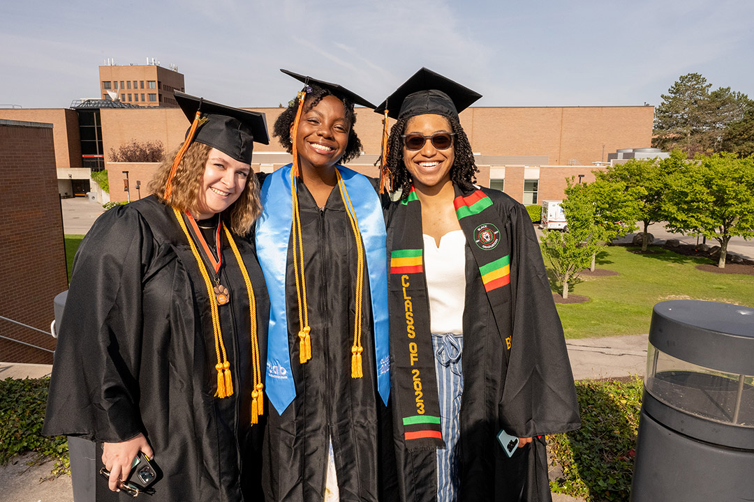 three graduating college students wearing their regalia.