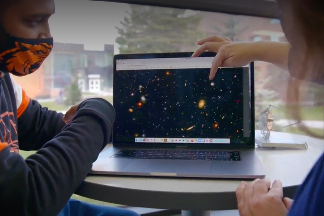 person pointing to stars in space on a laptop screen.