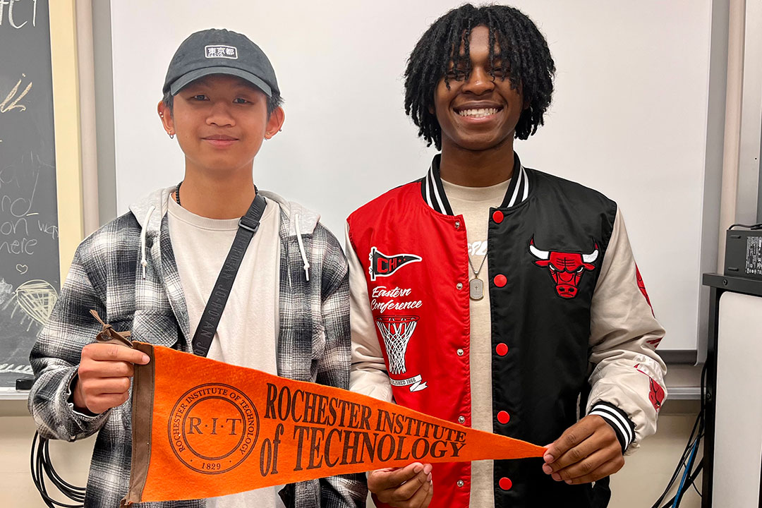 Two boys standing next to each other and holding a RIT sign