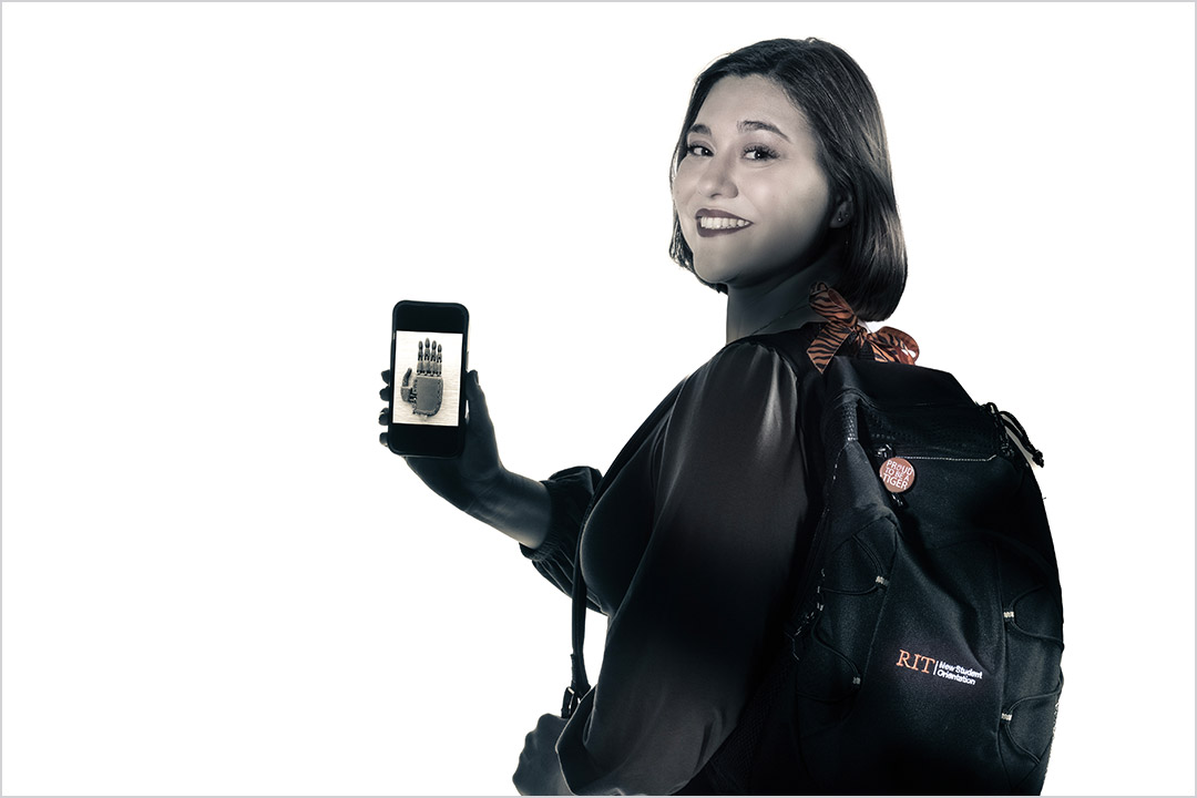 college student wearing a backpack and holding a smartphone that shows a picture of a prosthetic hand.