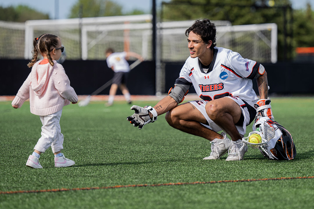 little girl walking up to a college lacrosse player on the field.