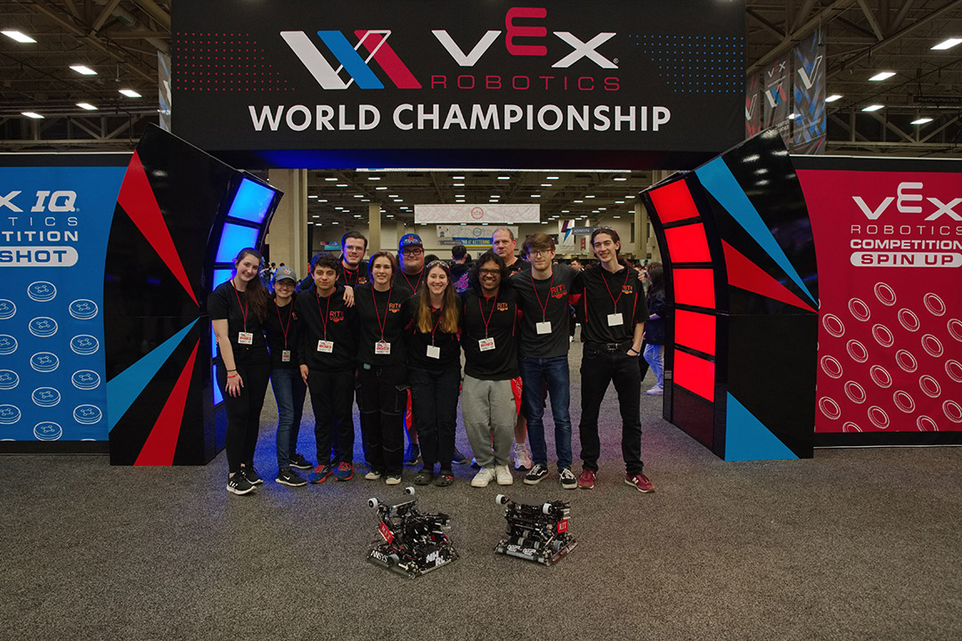 team of college students standing under a sign that reads, VEX Robotics world championship.