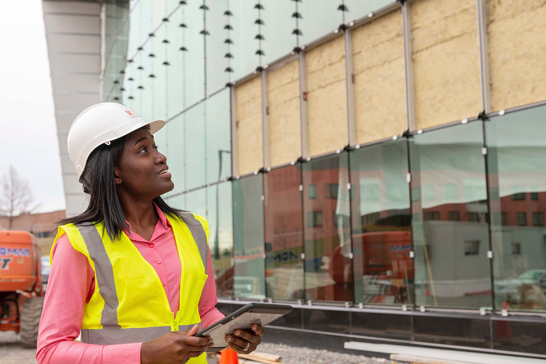 professor standing outside a building wearing a high-visibility vest and a hard hat.