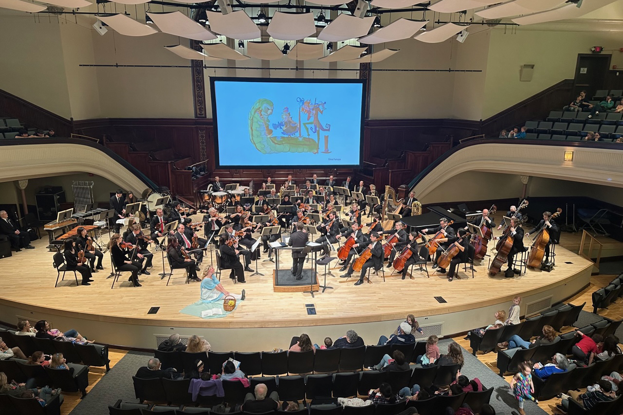 An orchestra plays a concert with a projected illustration by an RIT student on a screen.