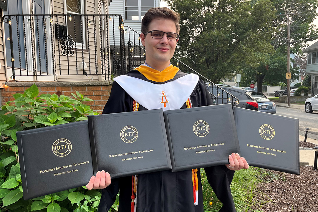 student wearing graduation regalia and holding four degree portfolios.