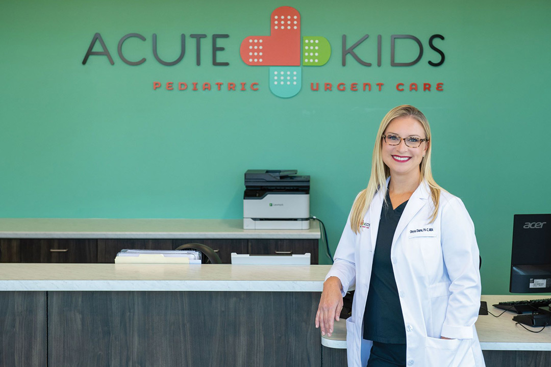 A woman stands in front of the AcuteKids Pediatric Urgent Care sign. 
