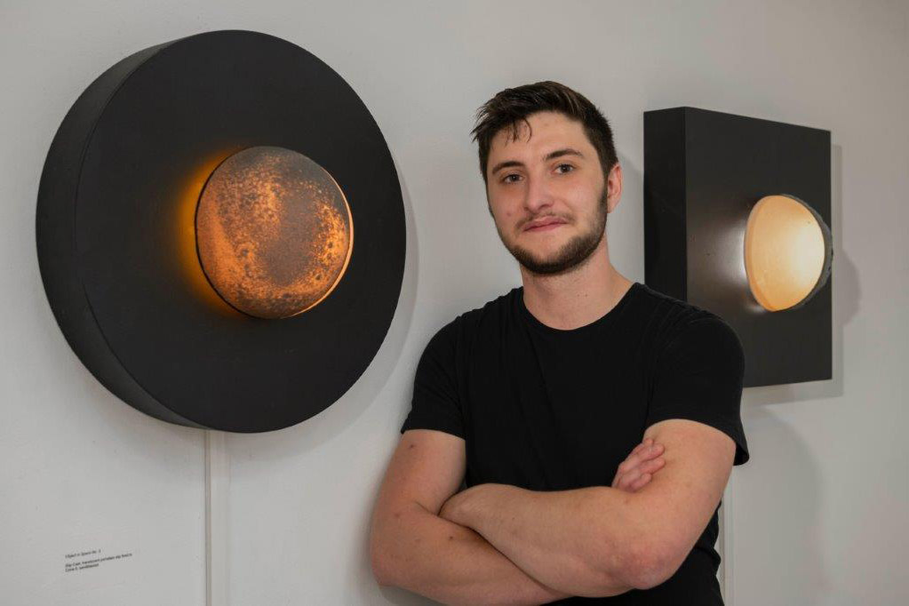 artist standing next to a round, translucent sconce. 