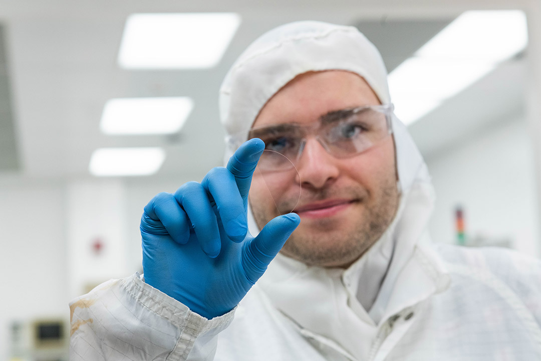 person wearing a clean suit holding up a thin piece of glass in the shape of a semicircle.