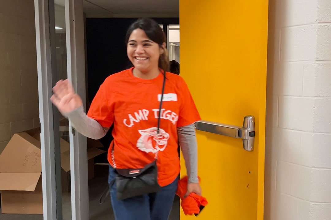 Girl waving and wearing an orange shirt