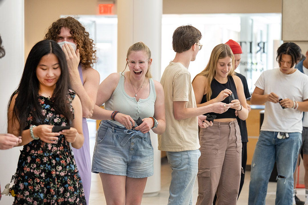 seven college students with surprised expressions standing in a line holding small black envelops.