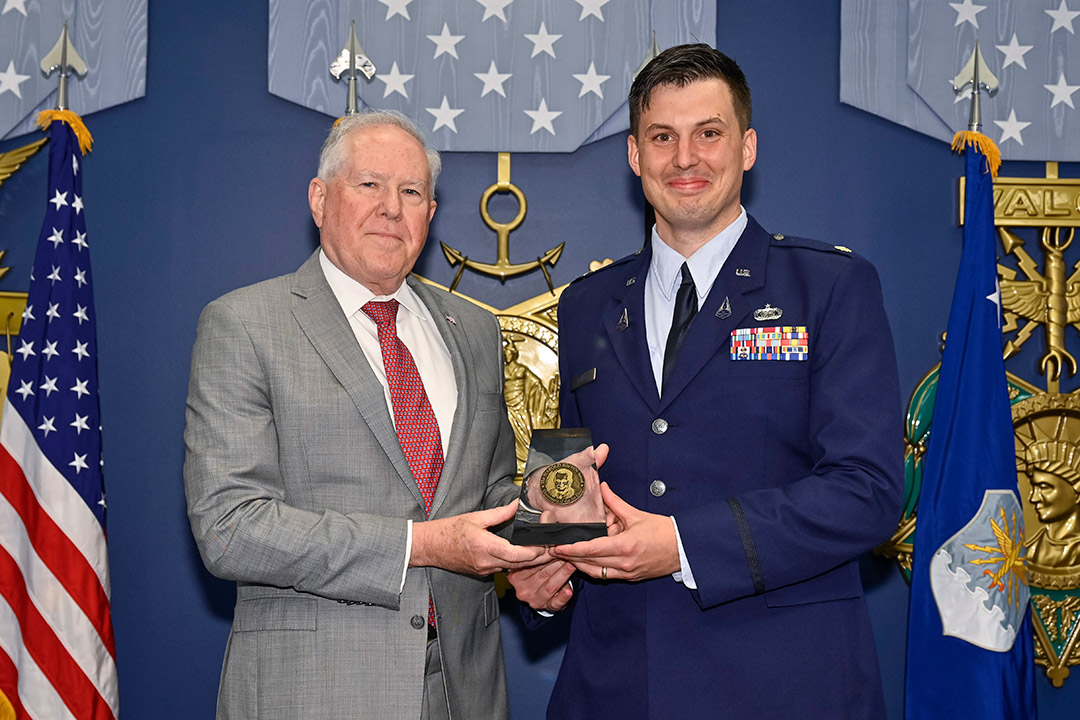 man in suit and man in an Air Force dress uniform holding an award.