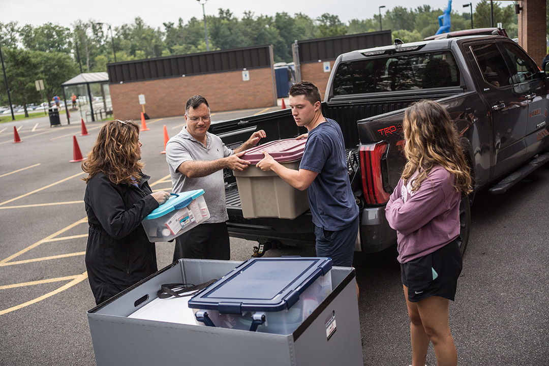 a father, mother and sister help a college student unload totes from a pickup truck.