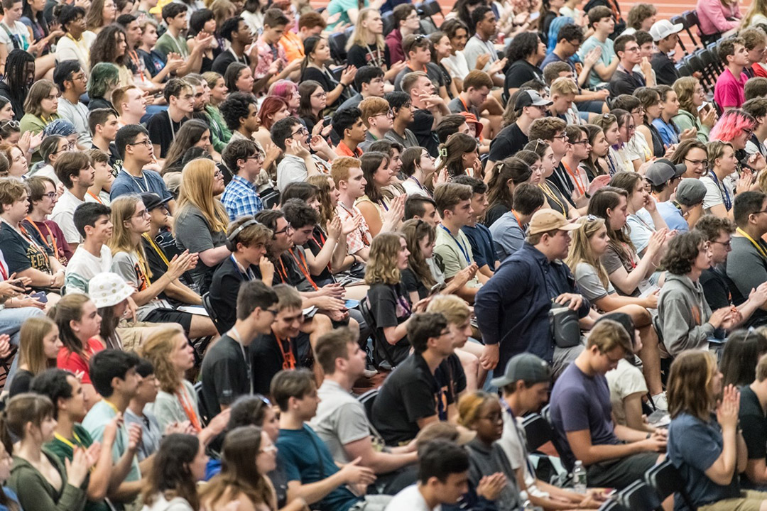 a crowd of college students sitting in folding chairs in a field house.