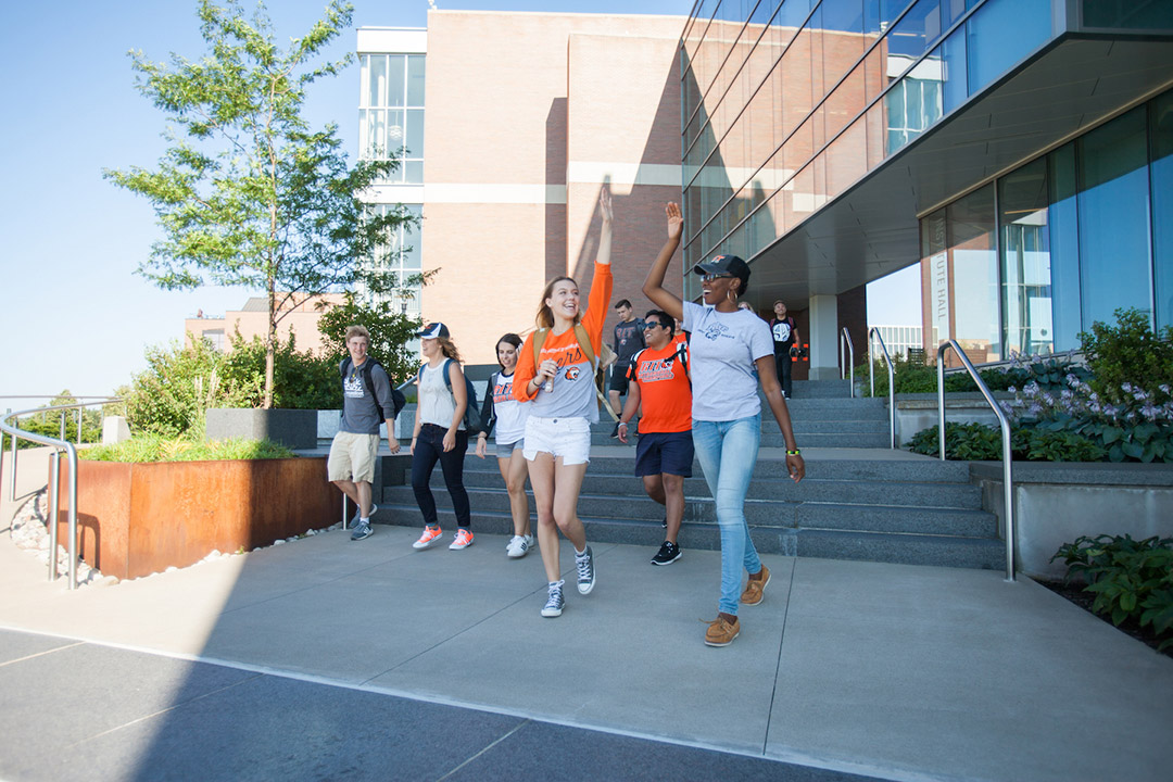 college students walking down a stairway outdoors, with two students high-fiving.