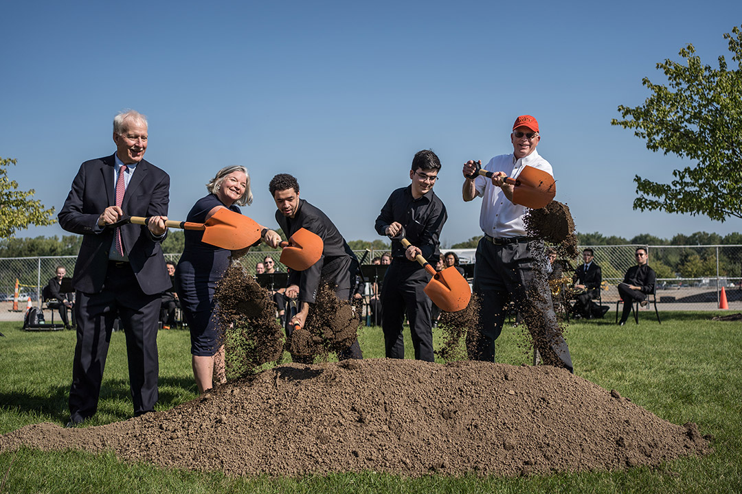 five people holding orange shovels at a ceremonial ground breaking.