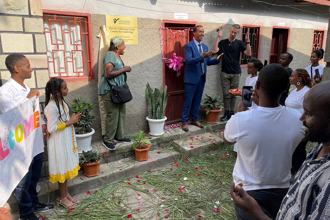 a crowd watching as a woman stands looking surprised next to two men making an announcement in front of a building in Ethiopia.