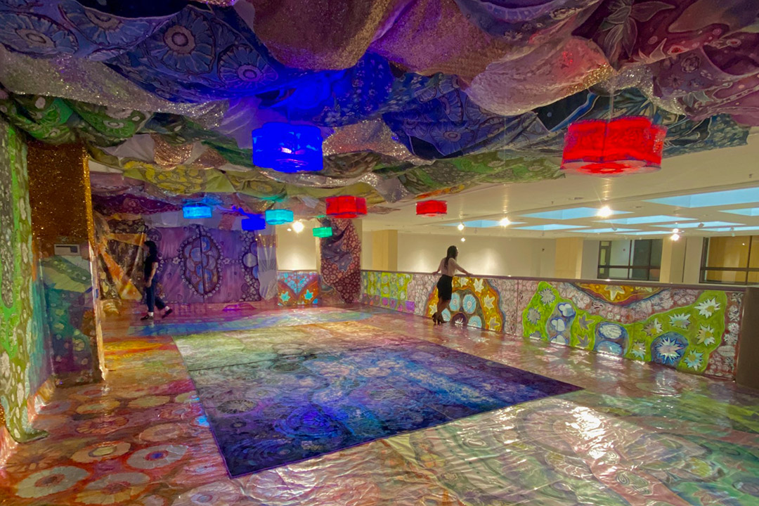 art exhibit with colorful floral coverings on the walls, floor, and ceiling of an upper level room.