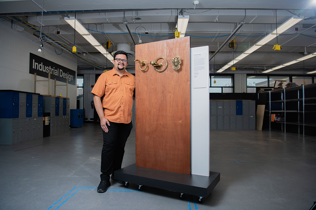 college professor standing next to a door-like display with three bronze door knockers mounted on it.