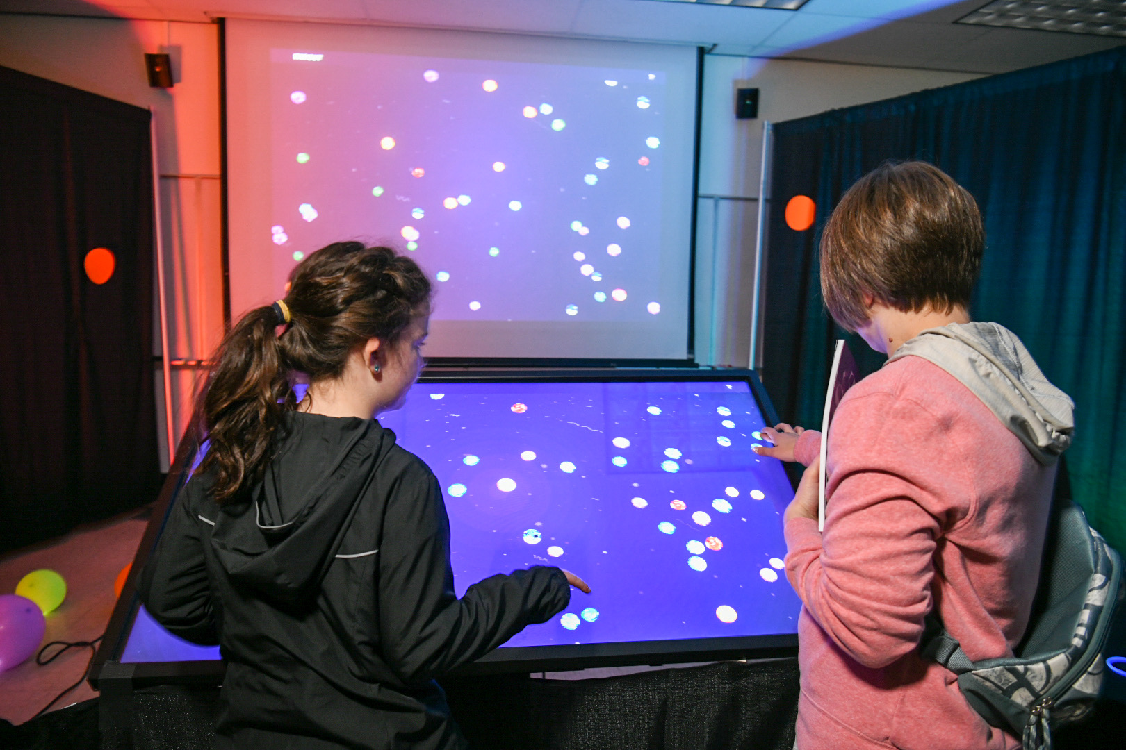 Two people interact with a digital display on a large screen.