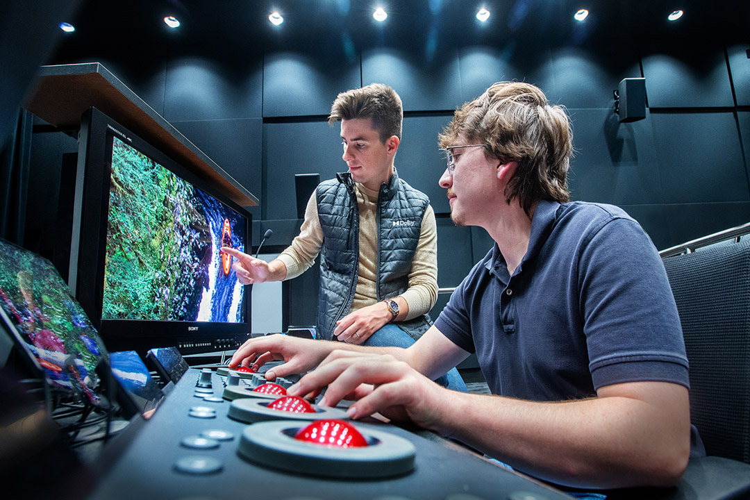 two men using round red joysticks looking at a colorful image on a T V screen.