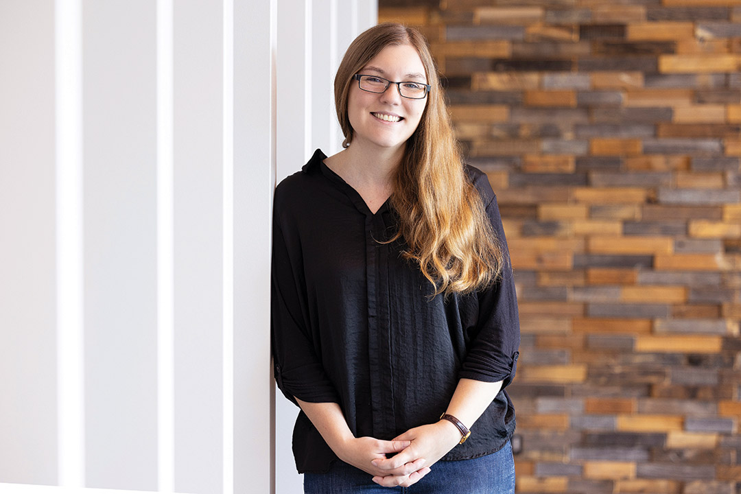 woman smiling and standing next to a white wall.