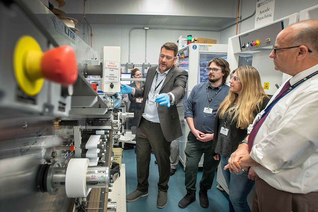 researcher showing three people a machine that processes batteries.