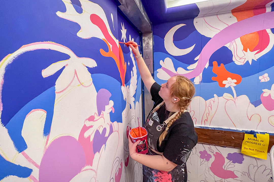 college student painting a mural of flowers and dragons in an elevator.
