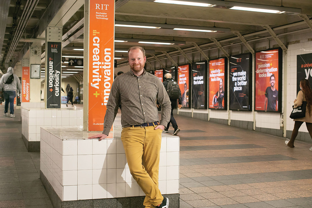 person standing in a subway station with ads for R I T all over the walls.