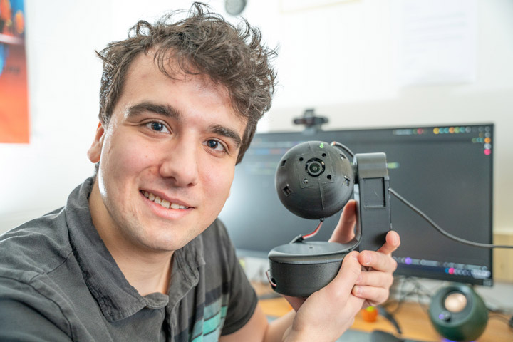 college student holding a small robot with a base and a ball component.