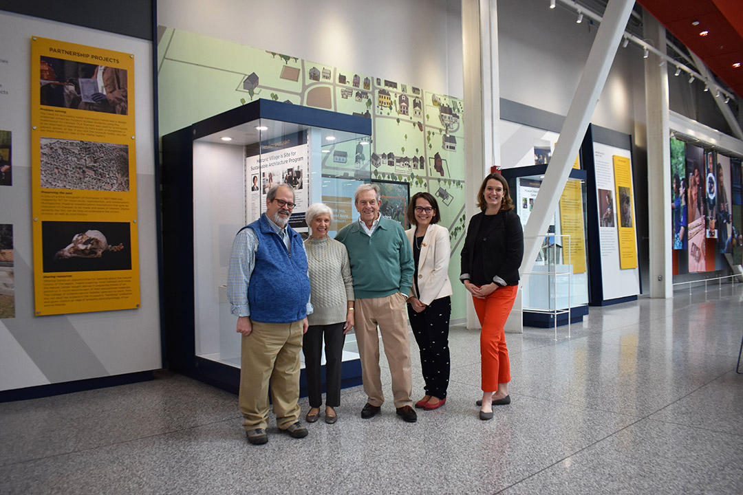 five people standing next to an art exhibit with floor to ceiling displays of maps and images.