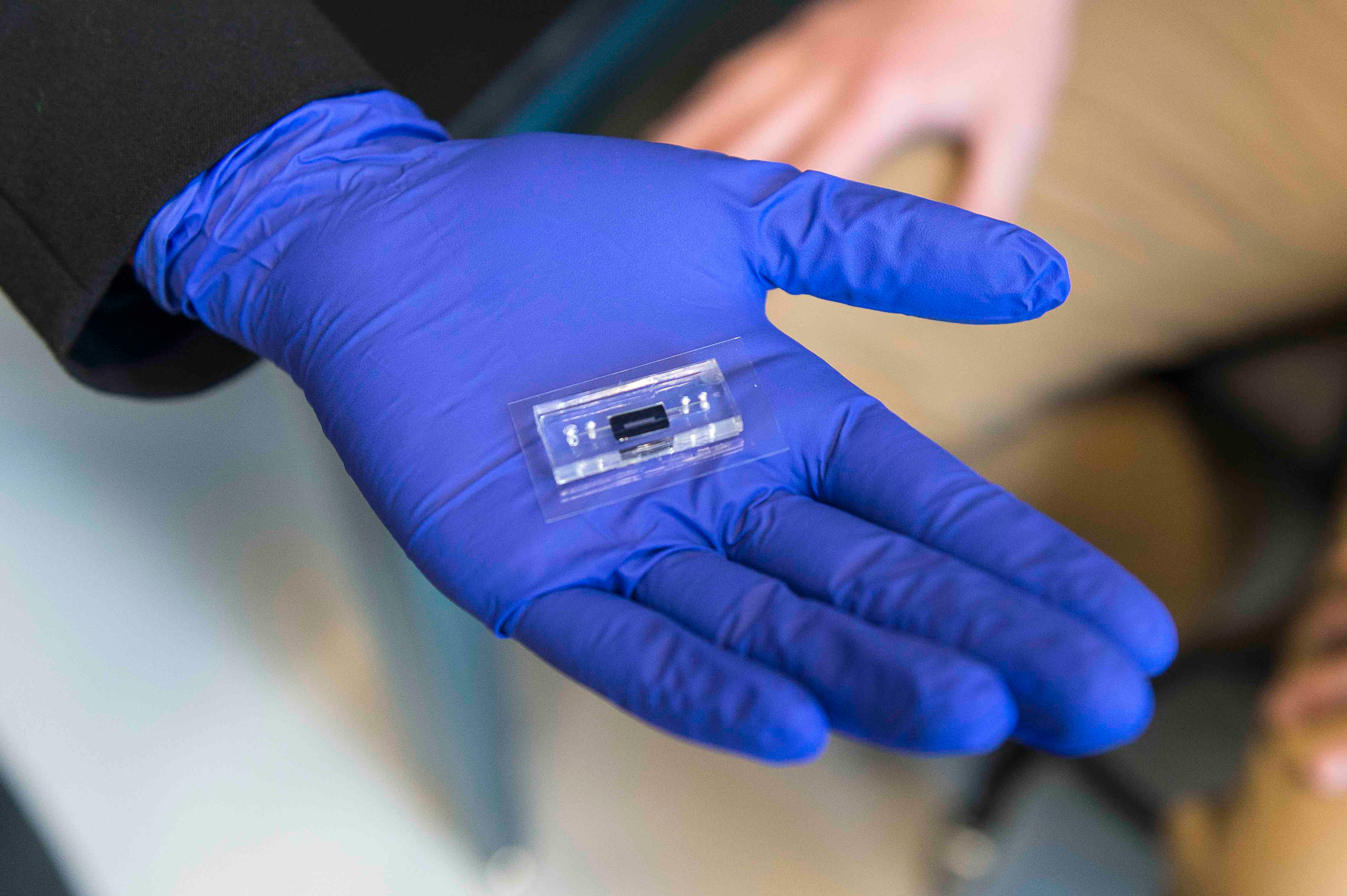 a microfluidic device used for data storage on DNA is sitting on a blue glove covered hand.