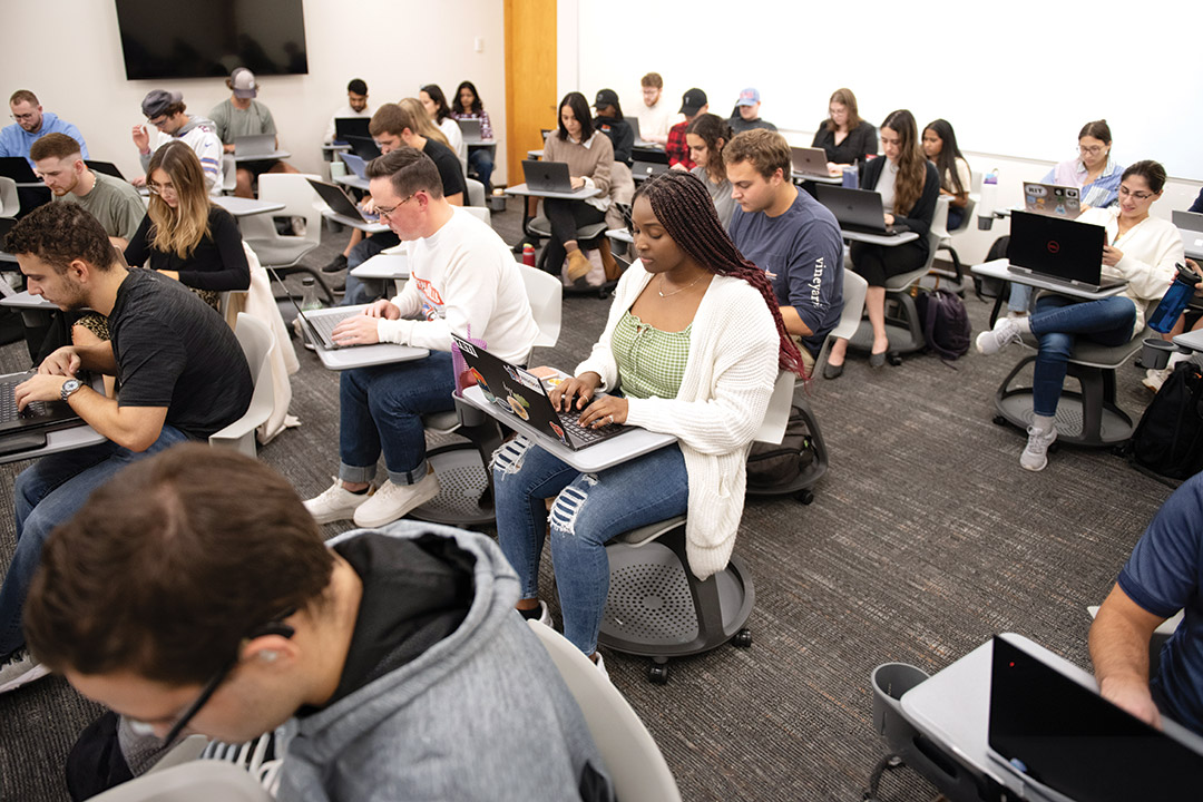 college students seated at individual desks working on their laptops.