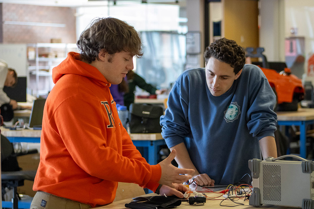 two students appear at a workshop table discussing a blood pressure cuff that is hooked to electronic instruments