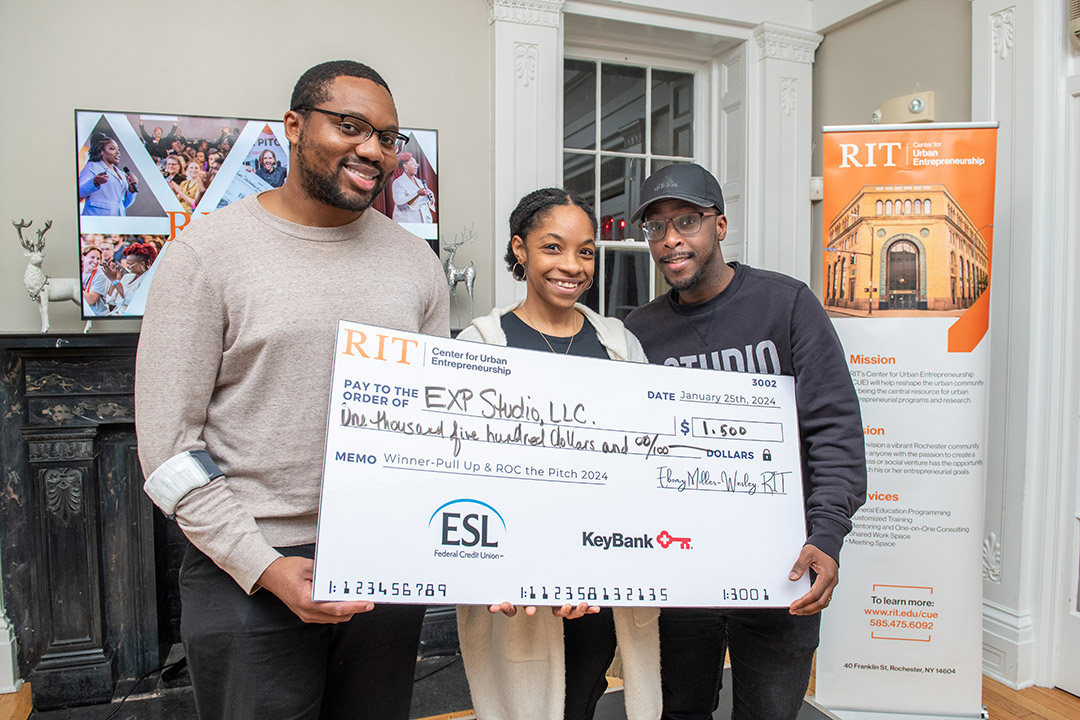 Business owners Jamal Henderson, Alexis Russell, and Antwan Russell are shown holding a large check for $1,500. 
