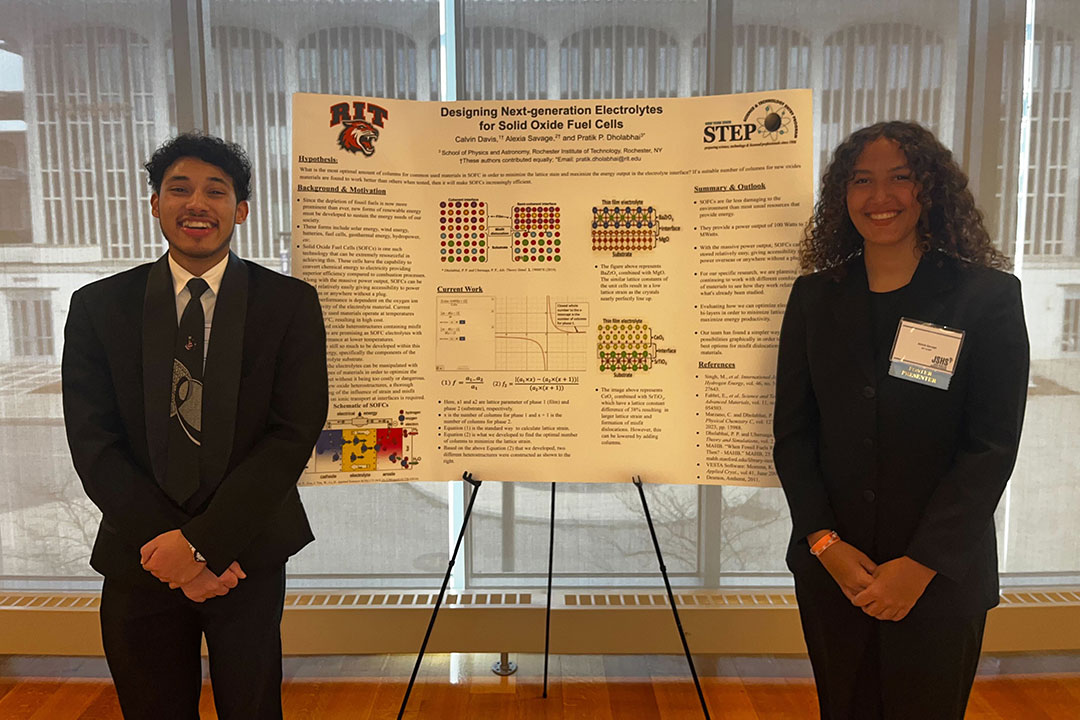 Two high school students standing next to a research poster