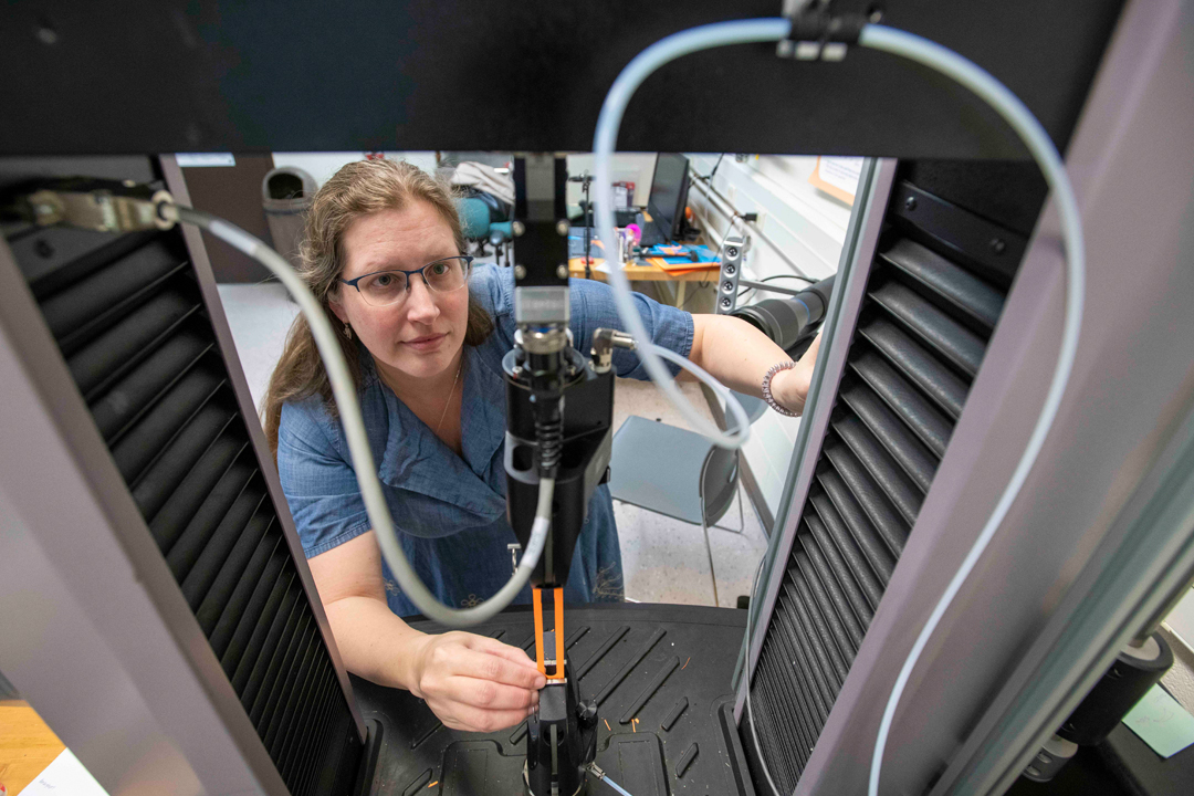 A woman with glasses looks into a machine with wires and instruments